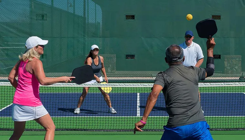 Two couples playing mixed doubles pickleball on an outdoor court